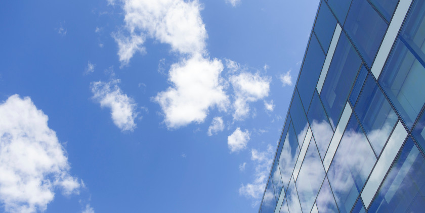 Cloud-Computing auf dem Bild ein blauer Himmel mit Wolken, rechts ein Hochhaus mit verspiegelter Fassade